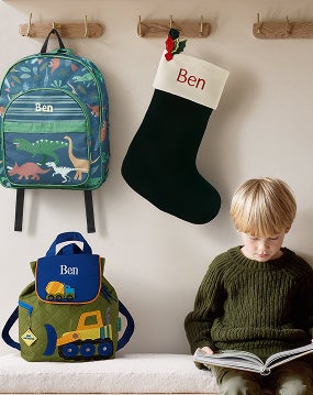 Boy reading surrounded by Mongrammed stocking and two backpacks